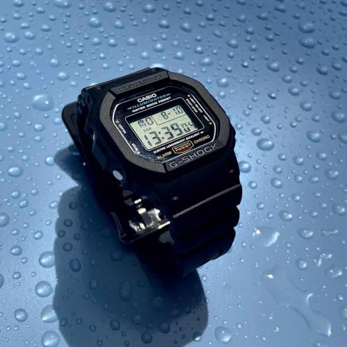 Наручные часы CASIO G-SHOCK DW-5600E-1VER, водозащита 200 метров, на синем фоне с каплями дождевой воды, фото вживую.